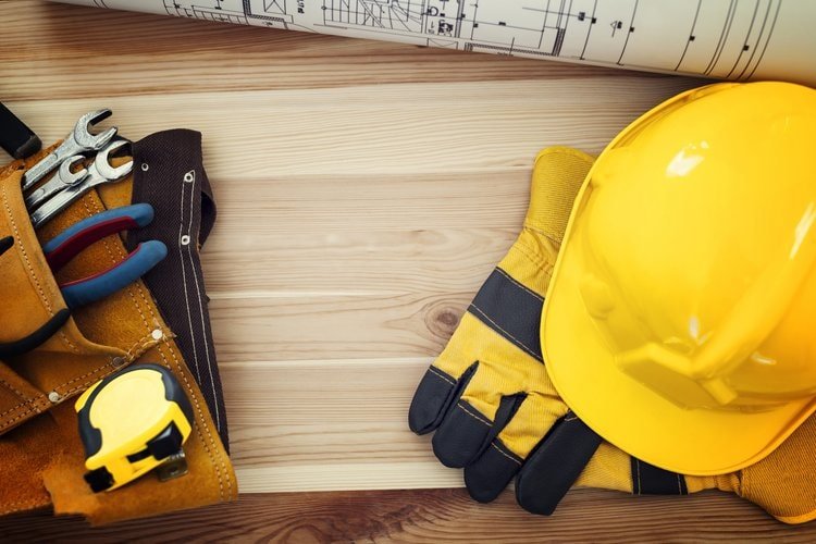 Yellow hardhat, gloves and a toolbelt sitting on a plank of wood